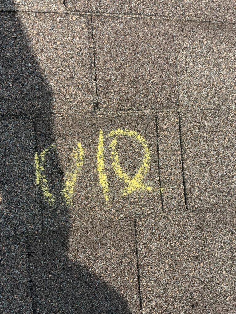 Yellow chalk marking beside a hail impact on an asphalt shingle