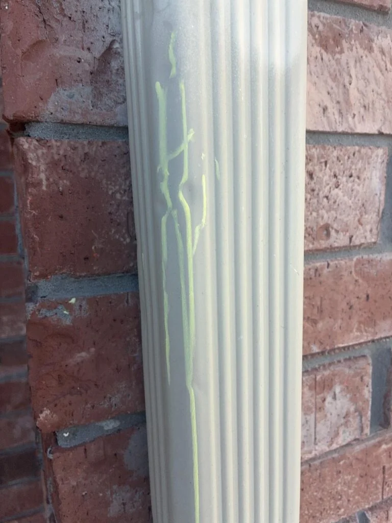Chalk-revealed hail dents running down an aluminum downspout