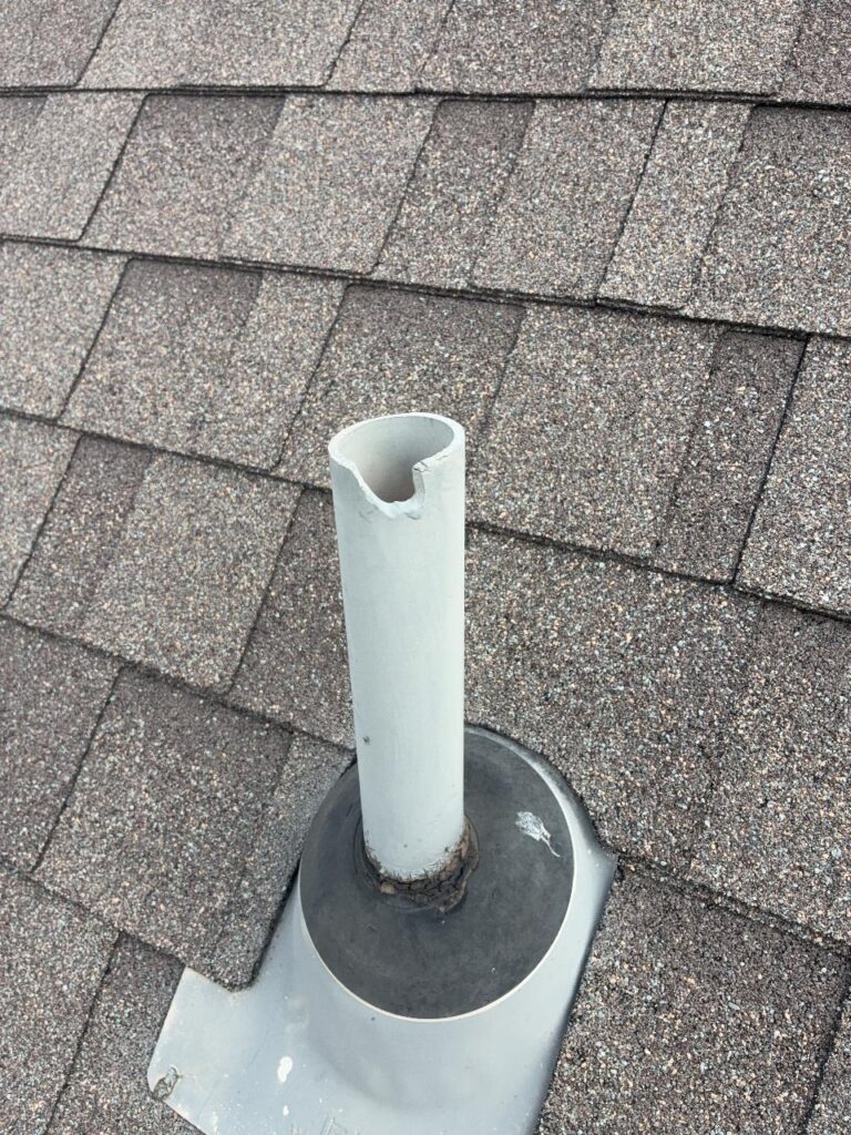 PVC plumbing vent pipe with a chip broken out of its rim, and cracked sealant where the pipe meets its flashing boot
