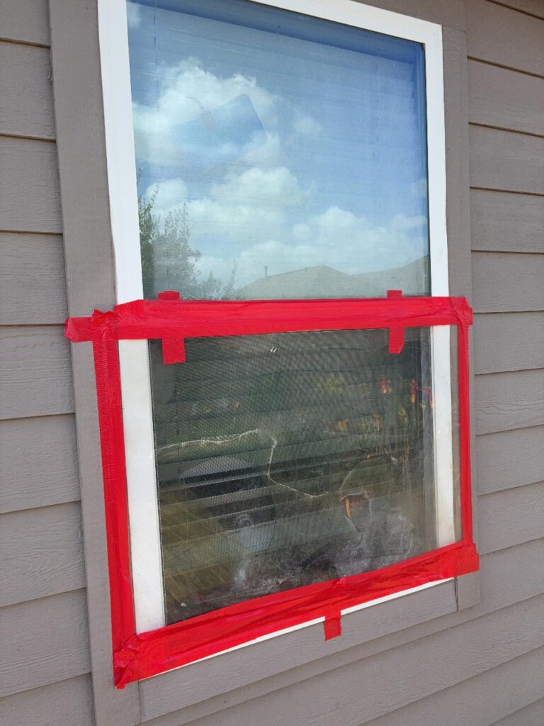 Window with a cracked lower sash taped shut after hail damage