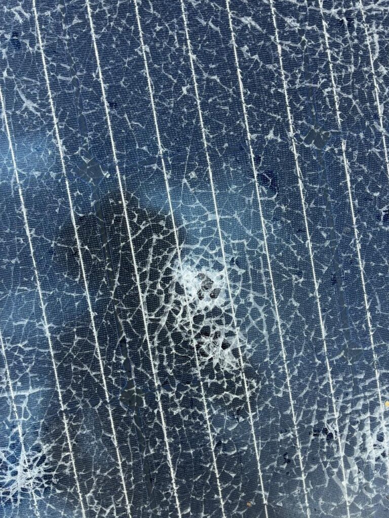 Close-up of a solar panel's tempered glass shattered around a hail strike