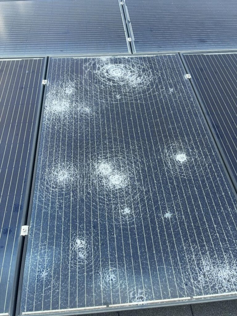 Shattered rooftop solar panel showing more than a dozen separate hail impact rings