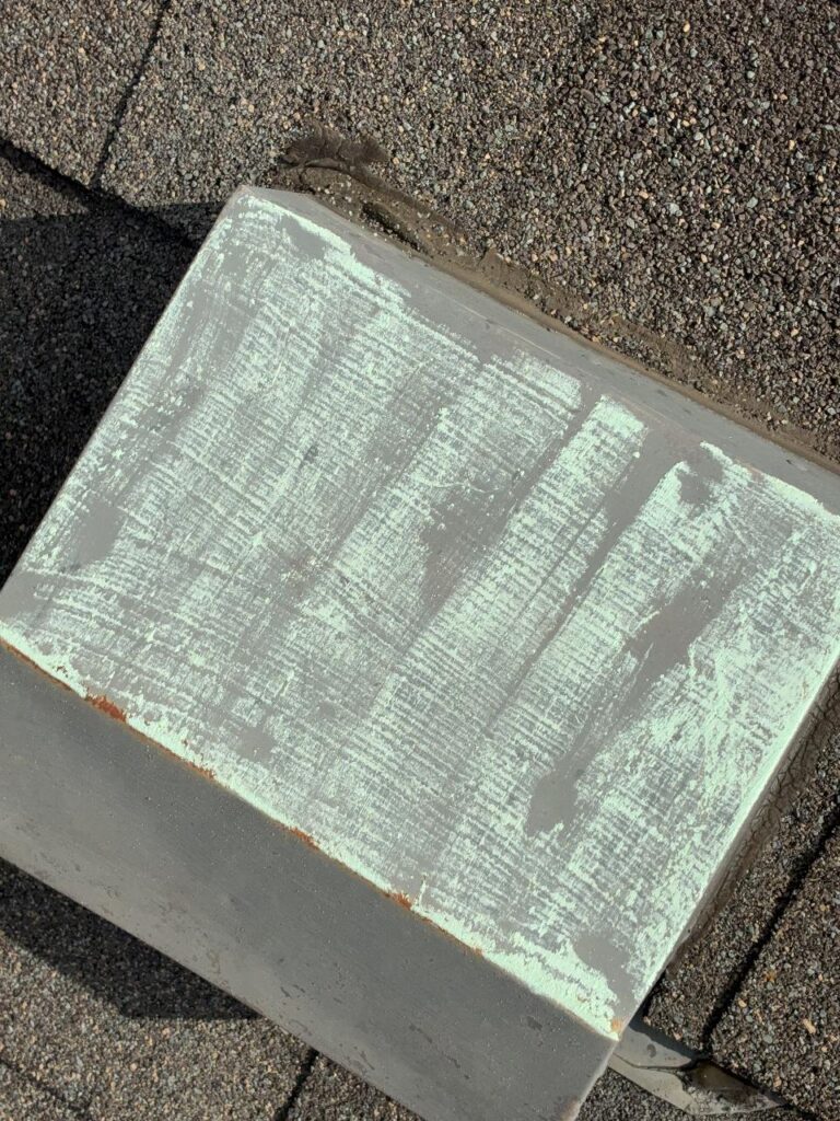 Chalk rubbed across the top of a metal roof vent, revealing scuffed impact marks in the soft metal