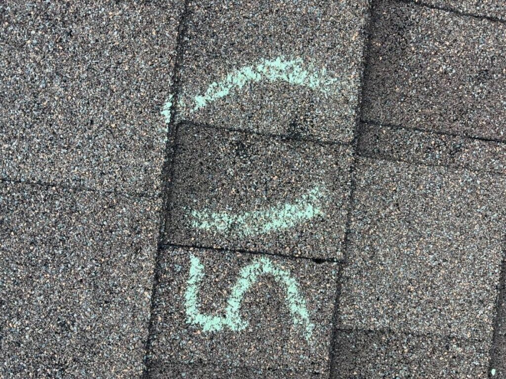 Hail impact marked in chalk on an asphalt shingle, with a second mark on the course above