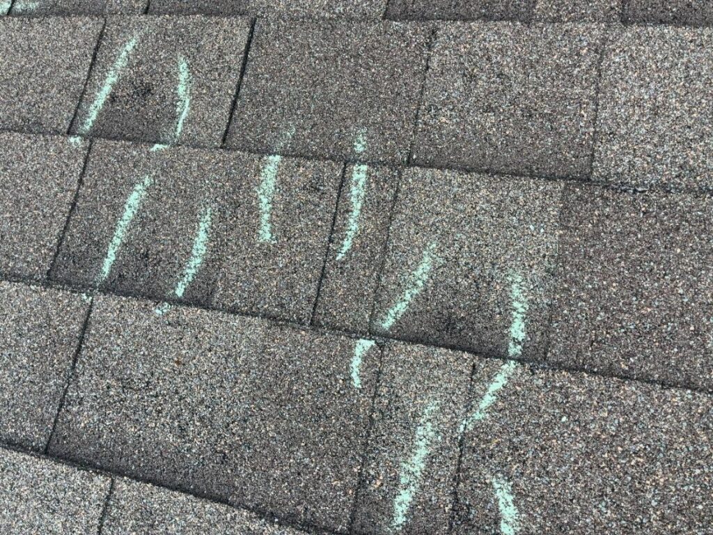 Chalk marks recording repeated hail strikes across several courses of asphalt shingles