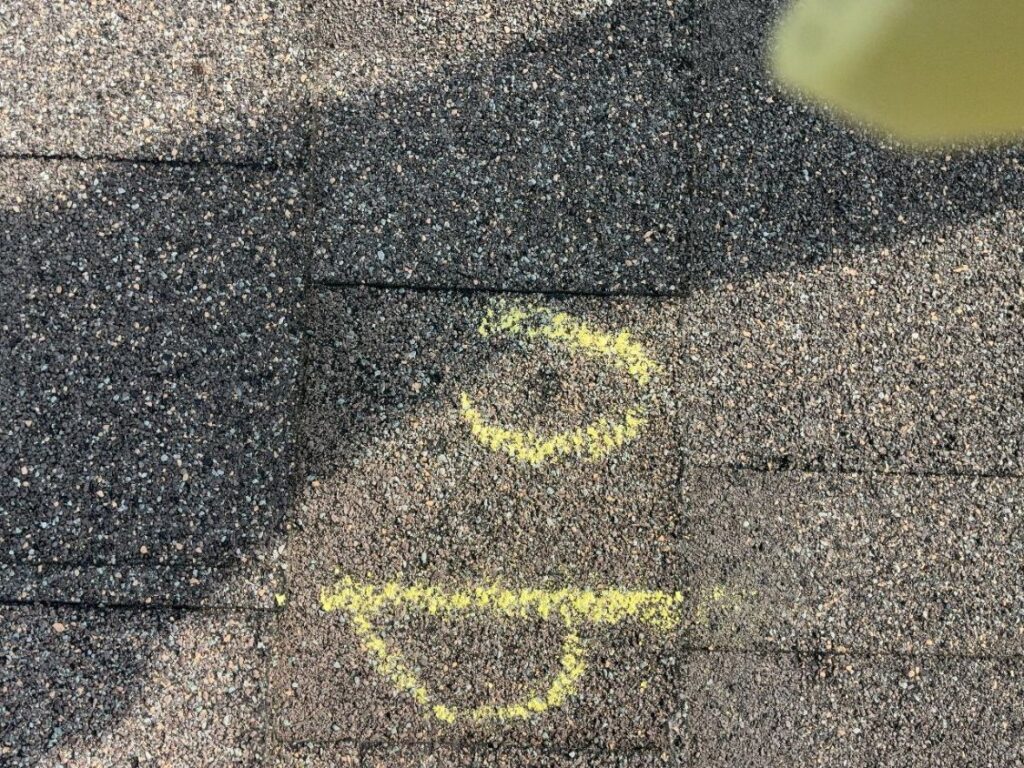 Two hail impacts circled in yellow chalk on weathered asphalt shingles