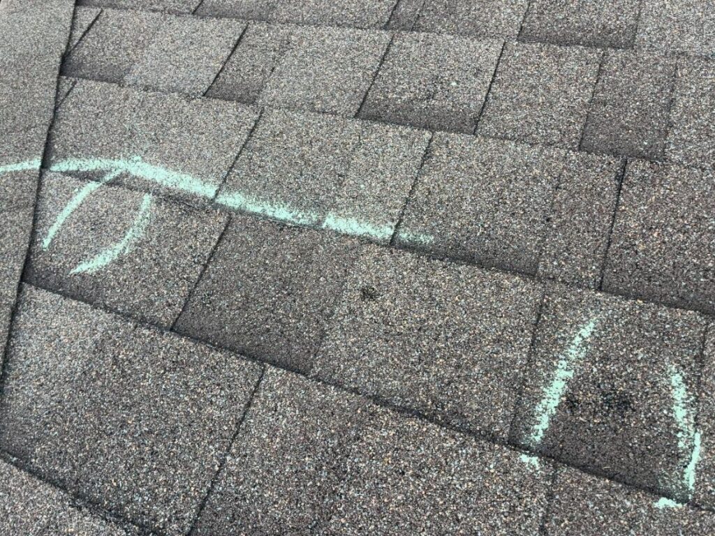 A chalk line bounding a marked test area on an asphalt shingle roof, with hail impacts circled inside it