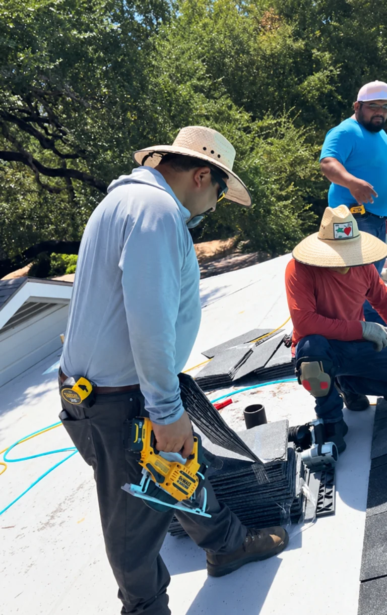 Construction workers on a sloped roof, one man in a light blue hoodie holding a yellow nail gun near bundles of roofing shingles.