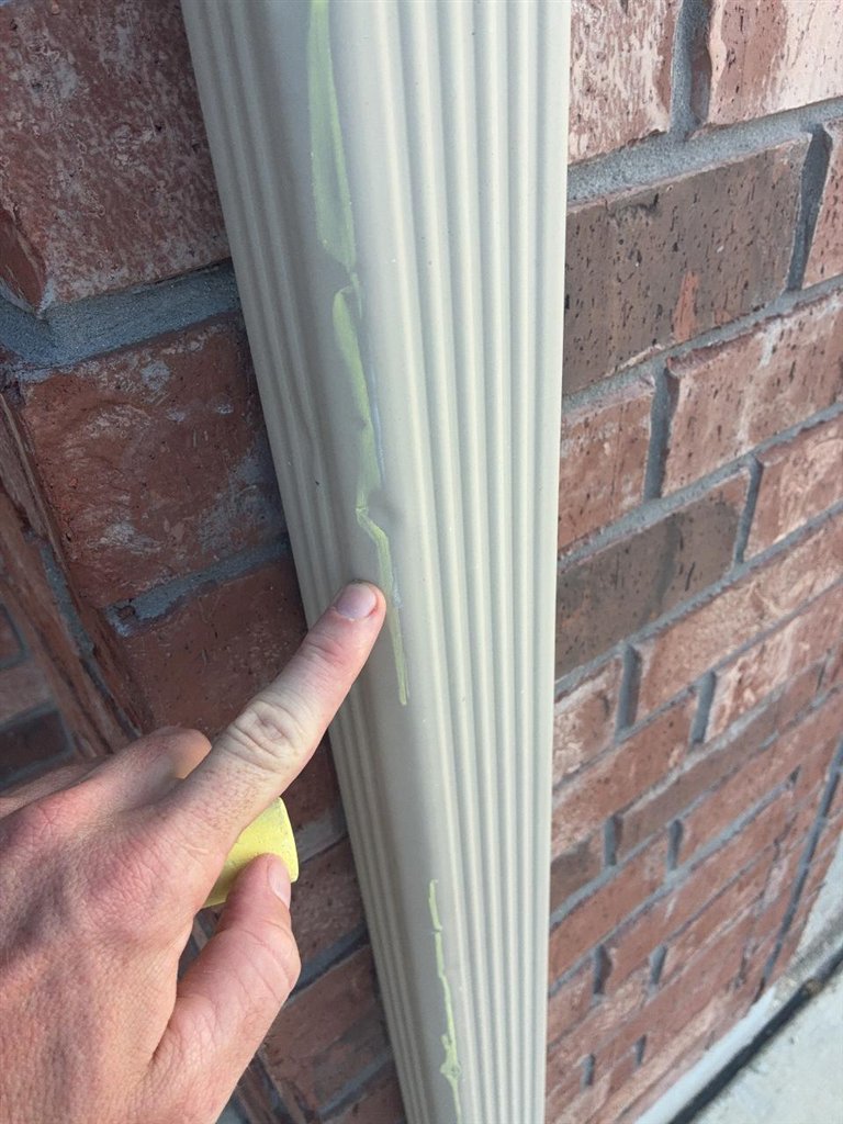 Inspector indicating chalk-highlighted dents on a downspout beside a brick wall on a Schertz, Texas home