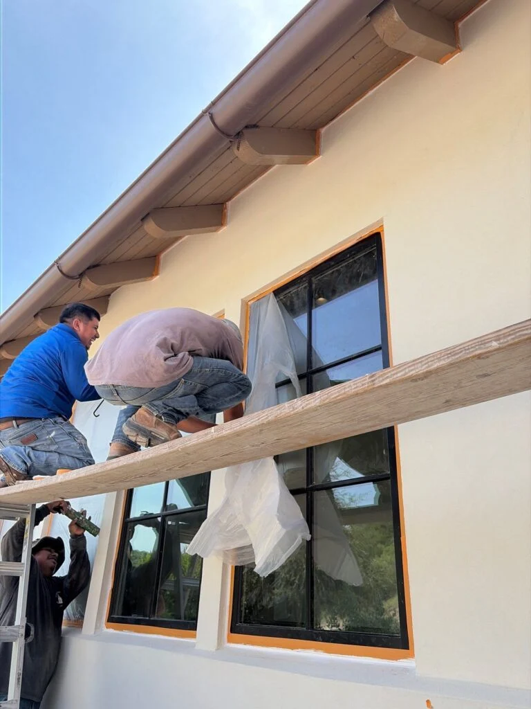 Driftwood Builders Roofing crew masking windows and trim to prepare James Hardie siding for painting on a Westlake, Austin project