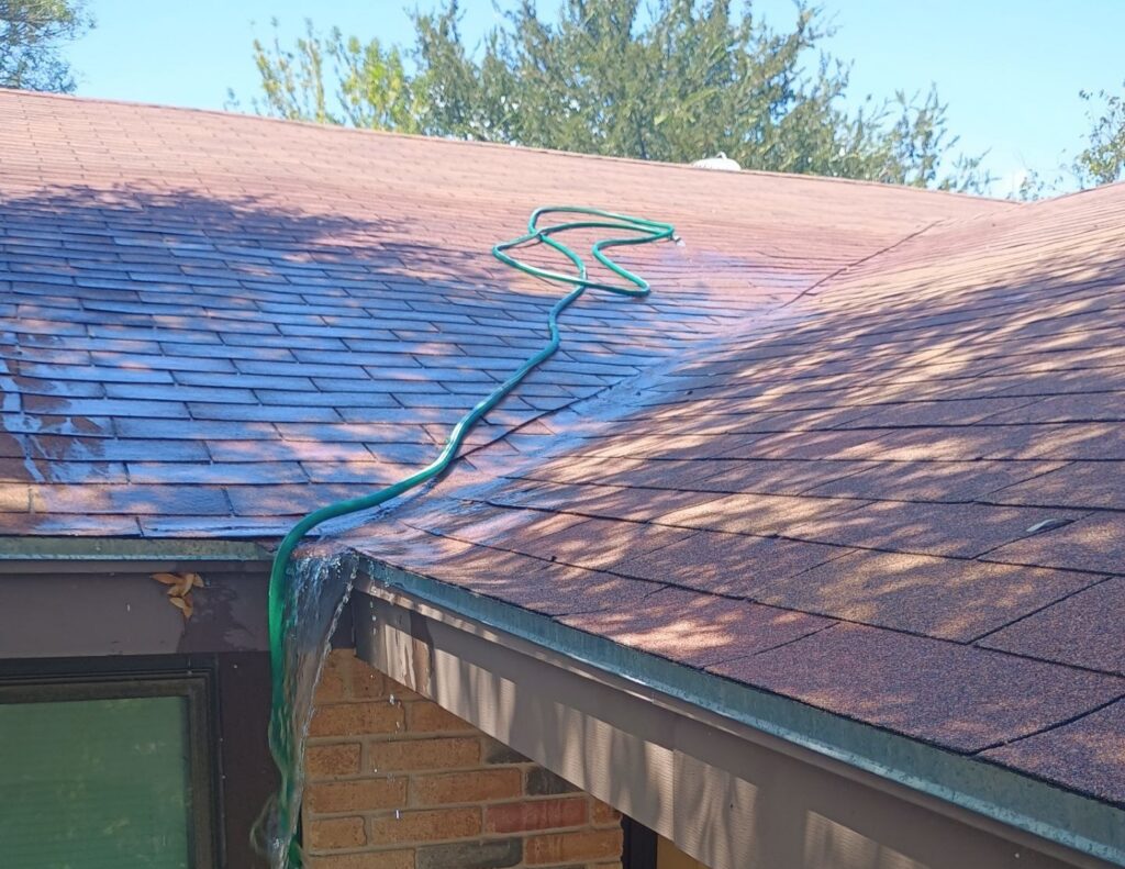 Garden hose running water down a repaired roof valley, with the water sheeting off the eave above the front entry
